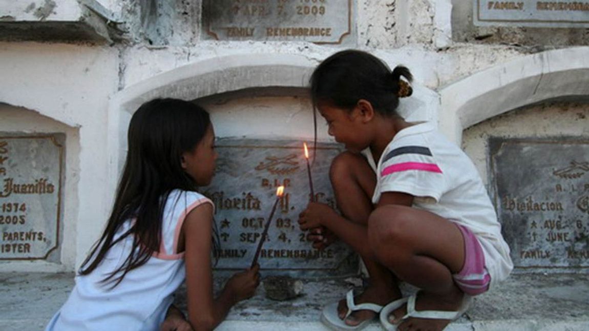 Philippinische Mädchen mit angezündeten Kerzen vor einem Grab
